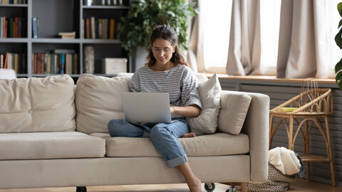 Frau sitzt mit Laptop auf der Couch