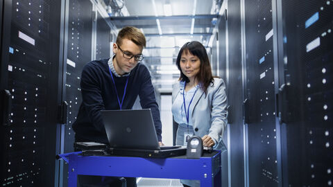 Mann und Frau vor einem Computer in einem Serverraum Mann und Frau vor einem Computer in einem Serverraum