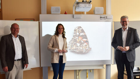 : Erster Kreisbeigeordneter Oliver Grobeis, Landtagsabgeordnete Sandra Funken und Staatssekretär Patrick Burghardt stehen nebeneinander bei der Übergabe und lächeln in die Kamera.