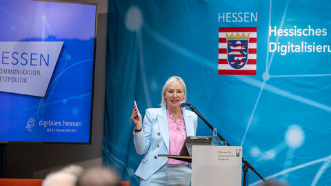 Digitalministerin Prof. Dr. Kristina Sinemus auf Bühne vor blauem Hintergrund mit Hessen-Logo
