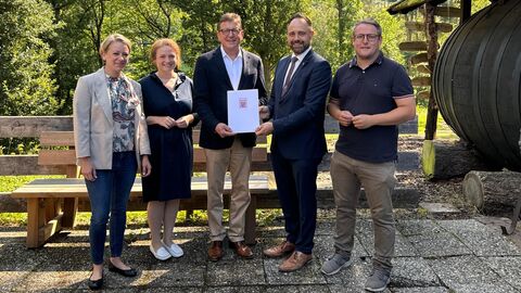 Staatssekretär Sauer steht mit mehreren Personen zusammen. Er hält den Zuwendungsbescheid in Händen.