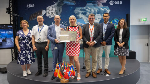Digitalministerin Prof. Dr. Kristina Sinemus zu Besuch bei der Esa Digitalministerin Sinemus steht mit einer Gruppe Personen auf einem Podest. Im HIntergrund ist ein BIld eines Satelliten und das Logo der esa zu sehen.