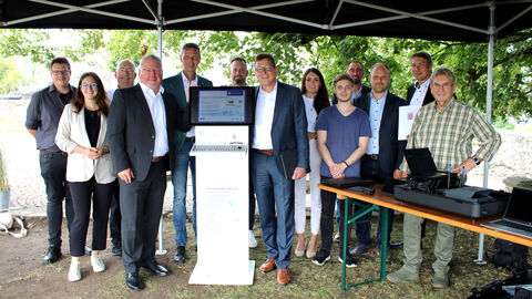 Staatssekretär Stefan Sauer steht mit weiteren Personen um ein Podest mit integriertem PC.