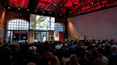 Frau steht auf Bühne und spricht zu Publikum.