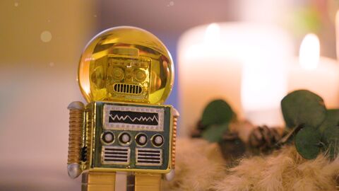Ausschnitt aus dem Videogrußwort der Ministerin: Kleiner goldener Roboter vor einem Adventskranz, bei dem 4 Kerzen brennen.