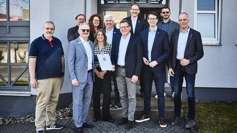 Staatssekretär Sauer steht mit weiteren Personen vor einem Gebäude und überreicht einen Förderbescheid.