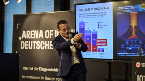 Ein Mann steht auf der Bühne mit einem Mikrofon in der Hand und zeigt mit der Hand zur Seite.