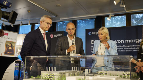 Drei Personen stehen vor einem Miniaturmodell von Gebäuden.