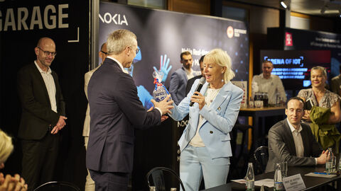 Ein Mann überreicht Digitalministerin Sinemus ein Präsent. Sie hält ein Mikrofon in der Hand und lächelt.