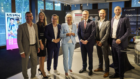 Sieben Menschen stehen in Anzügen nebeneinander und lächeln in die Kamera.