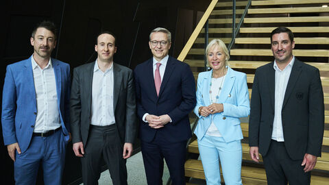Fünf Personen stehen nebeneinander und vor einer Treppe.