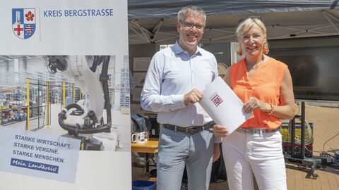 Ein Mann und eine Frau halten Förderbescheid mit Hessenwappen in die Kamera.