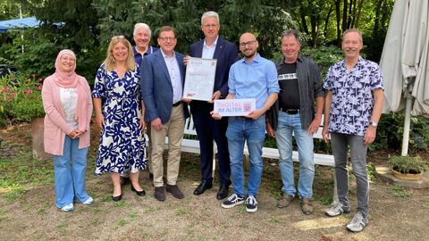 Mehrere Menschen stehen vor einem Baum und lachen in die Kamera.