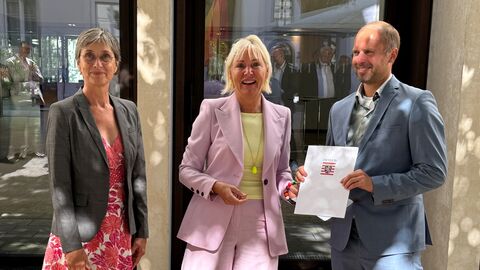 Dr. Sinemus steht mit einer Frau und einem Mann in einer Reihe - der Mann hält einen Förderbescheid in den Händen.