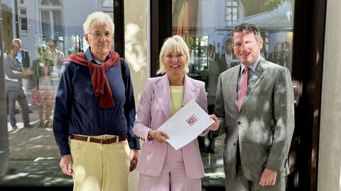Dr. Sinemus steht mit zwei Männern in einer Reihe - sie hält einen Förderbescheid in den Händen.