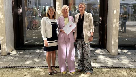 Dr. Sinemus steht mit zwei Frauen in einer Reihe - sie hält einen Förderbescheid in den Händen.