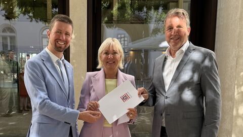Dr. Sinemus steht mit zwei Männern in einer Reihe - sie hält einen Förderbescheid in den Händen.