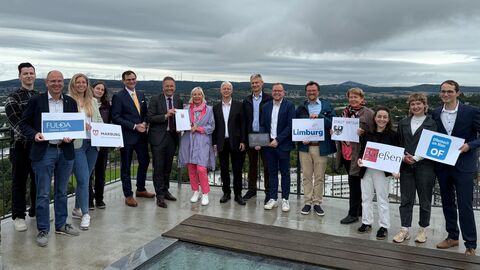 Interkommunale Zusammenarbeit der Städte Fulda, Gießen, Limburg, Marburg, Offenbach und Wetzlar Mehrere Personen stehen auf Balkon. Im Hintergrund sieht man eine Stadt und Berge.