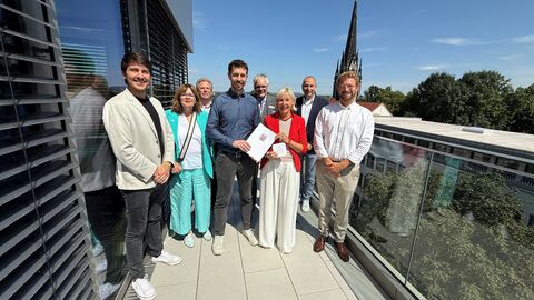 Förderbescheid Veli GmbH Digitalministerin Sinemus übergibt einen Förderbescheid, während die Gruppe auf einem Balkon steht.