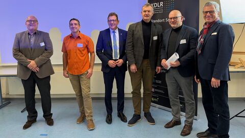 Sechs Männer stehen nebeneinander. Hinter ihnen ein Aufsteller mit der Aufschrift "KDLR".