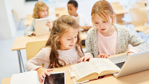 Zwei Mädchen in der Schule über Buch und PC